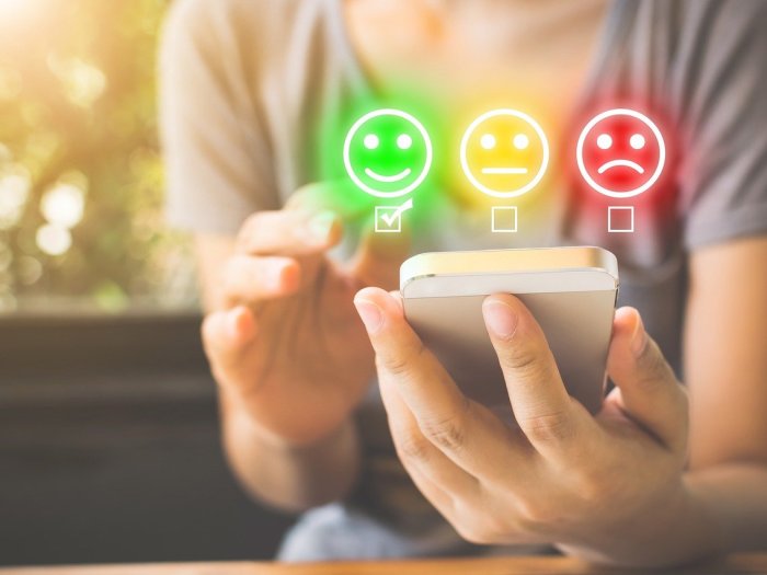 Hands holding and using a smartphone. A green smiling face, a yellow neutral face, and a red frowning face are superimposed over the top.