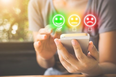 Hands holding and using a smartphone. A green smiling face, a yellow neutral face, and a red frowning face are superimposed over the top.